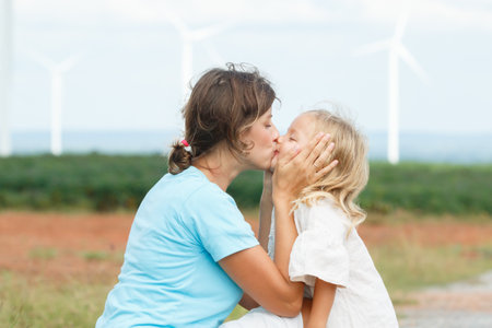 Happy and cheerful caucasian - white woman and little daughter are playing and walking together in nature with the beautiful windmills landscape in background. Mom is taking care of her daugher.の写真素材