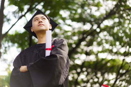 Male student in graduation gown has an excited and delighted expression as he receive his diploma upon graduating from university. An Asian student feel proud about academic achievement.の写真素材
