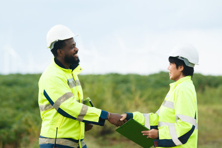 Team of electricians engineer are having a conversation and discussion together at electric generator windmill station. Female and male professional engineers are working at electric wind turbine.の写真素材