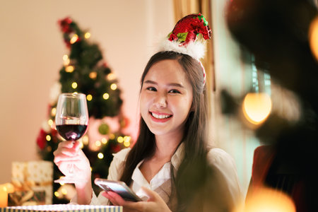 A beautiful Asian woman is excited to open Christmas presents during her Christmas dinner in a cozy and warm living room at home. She is enjoying celebrating Christmas night alone.の写真素材