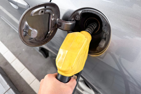Unrecognizable man refueling his car at self-service gas station, man refilling his vehicle gas at the gas station. Close up shot on a hand is catching on a gas dispenser while refuel a petrol.の写真素材