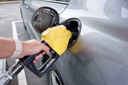 Unrecognizable man refueling his car at self-service gas station, man refilling his vehicle gas at the gas station. Close up shot on a hand is catching on a gas dispenser while refuel a petrol.の写真素材