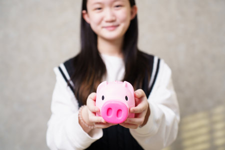 Asian girl happily shows her piggy bank and smiles at the camera. Learning about saving money and investing in children for a better future.の写真素材