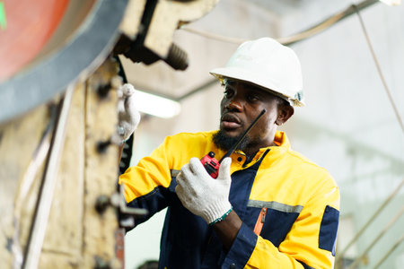 Smart and good looking African Black ethnicity male industry engineer performs inspection machines. Engineer is checking for the properly of machine system and working environment safety in factory.の写真素材