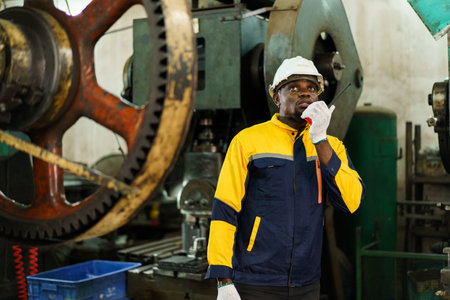 African Black ethnicity male industry engineer performs inspection machines. Engineer is checking for the properly of machine system and working environment safety in factory.の写真素材
