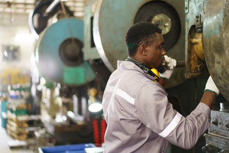 Smart African male industry engineer performs inspection machines. Engineer is checking for the properly of machine system and working environment safety in factory.の写真素材