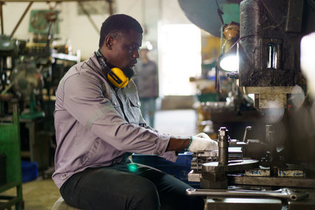 Smart and good looking African Black ethnicity male industry engineer performs inspection machines. Engineer is checking for the properly of machine system and working environment safety in factory.の写真素材