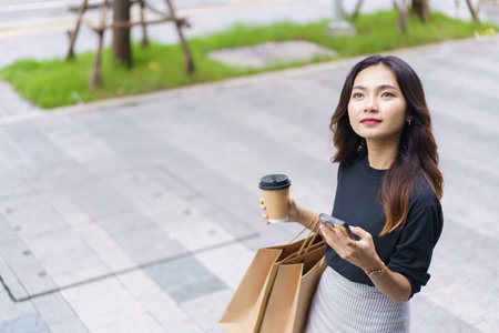 Smart and good looking Asian businesswoman is walking in the city while using a smartphone for text...