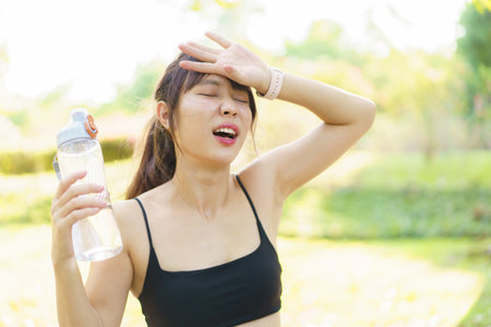 Asian slim fit beautiful woman drinking water from bottle during running at the park. Thirsty Asian...