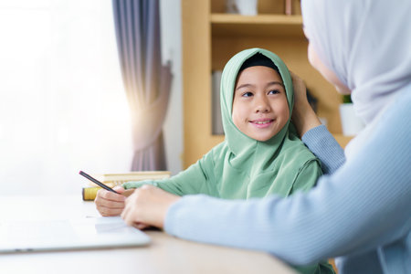 Asian Muslim woman is teaching and reviewing homework with her daughter in the evening after school, with great dedication. A modern muslim family and lifestyles concept.の写真素材