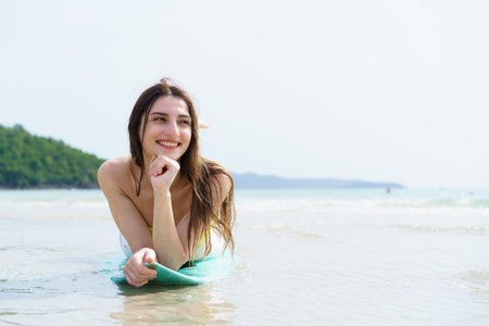 Good looking Western woman enjoys posing with a surfboard on a sunny beach day, capturing joyful summer moments and reflecting outdoor travel, freedom, and holiday relaxation by the ocean.の写真素材