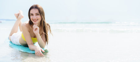 Good looking Western woman enjoys posing with a surfboard on a sunny beach day, capturing joyful...