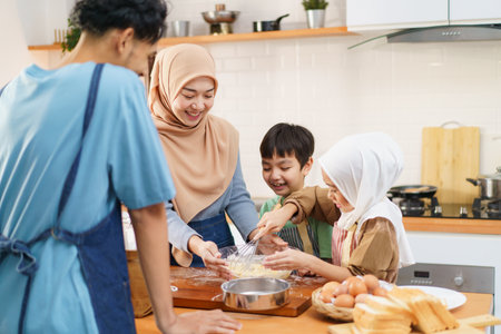 Happy - cheerful Asian muslim man and woman and children are mixing a flour on the kitchen counter together. Lovely Asian children assists her mother mother cooking in kitchen.の写真素材