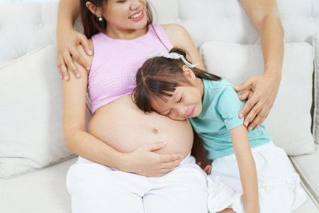 Asian family â€” husband, pregnant wife, and young daughter â€” relaxing and chatting...