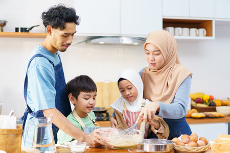 Happy - cheerful Asian muslim man and woman and children are mixing a flour on the kitchen counter together. Lovely Asian children assists her mother mother cooking in kitchen.の写真素材