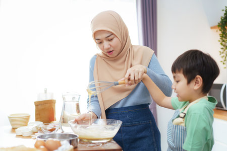 Happy - cheerful Asian muslim man and woman and children are mixing flour on the kitchen counter together. Lovely Asian children assist their mother cooking in the kitchen.の写真素材