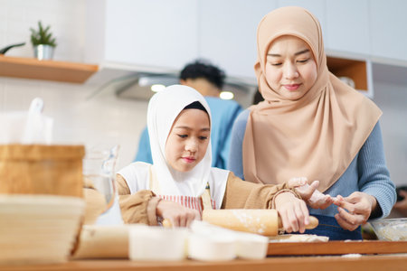 Happy - cheerful Asian muslim man and woman and children are mixing flour on the kitchen counter together. Lovely Asian children assist their mother cooking in the kitchen.の写真素材