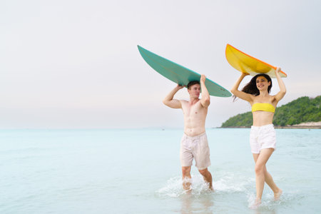 Caucasian couple are walking along the beach with surfboard together. They enjoy playing surf together in their romantic moment at the beach. Vacation and leisure activities.の写真素材