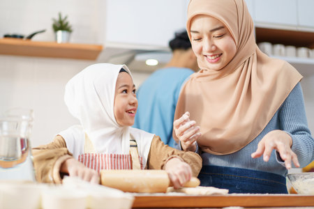 Happy - cheerful Asian muslim man and woman and children are mixing flour on the kitchen counter together. Lovely Asian children assist their mother cooking in the kitchen.の写真素材