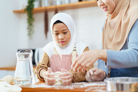 Happy - cheerful Asian muslim man and woman and children are mixing a flour on the kitchen counter together. Lovely Asian children assists her mother mother cooking in kitchen.の写真素材