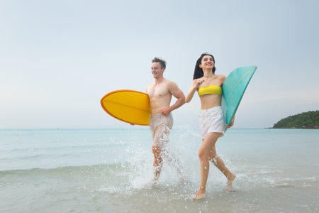 Good looking caucasian white couple are walking along the beach with surfboard together. They enjoy playing surf together in their romantic moment at the beach. Vacation and leisure activities.の写真素材
