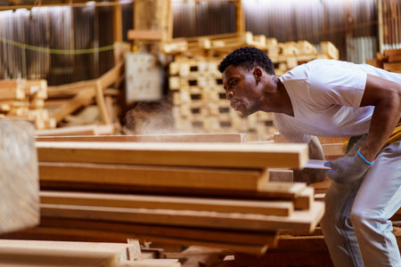 African carpenter works in a woodworking shop, using a tape measuring and pencil to mark on a wood...
