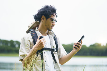 Asian man enjoys summer hiking, trekking, and camping in nature. While resting on the trail under...