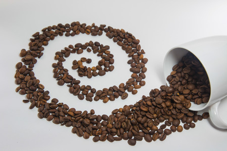 Spilled coffee beans from the white ceramic cup a beautiful pattern on white backgroundの写真素材