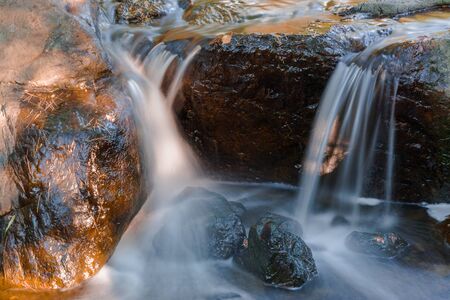 Water falls over a jumble of moss-covered boulders in forest.の写真素材