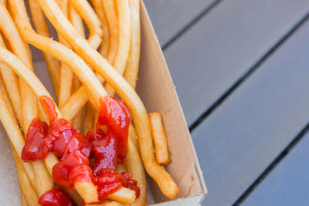 Long French fries potatoes in paper box on wood table ready to be eatenの写真素材