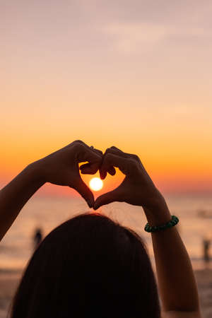 Silhouette Hands in shape of love heart at sunset. Female hands of heart against the sky pass sun beams, concept happy in loveの写真素材