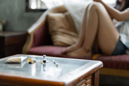 There are many drugs on the table with blur background of young Asia woman sitting on the sofa. hopeless conceptの写真素材