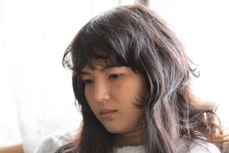 Young Asia girl sitting on the sofa feeling be absent-minded, Lonely girl conceptの写真素材