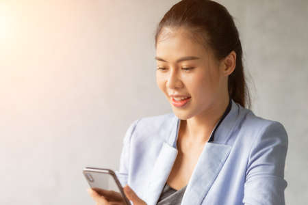 Close up portrait asian woman employee working in office looking on mobile phone with feeling successの写真素材