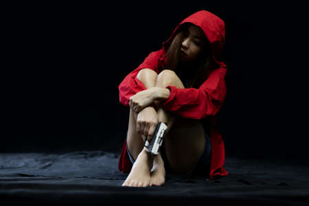 Hopeless Woman in violence with gun in hand sitting in dark room. The concept of stressed womanの写真素材