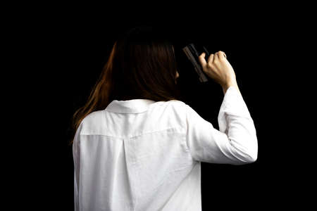 Teenager problems and crime concept. Asian woman portrait holding a gun and put the gun beside the body isolated on black background.の写真素材