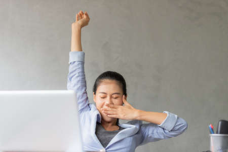 Business women or working lady are stretch oneself or lazily for relaxation on her desk while doing her work in the office.の写真素材