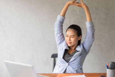 Business women or working lady are stretch oneself or lazily for relaxation on her desk while doing her work in the office.の写真素材