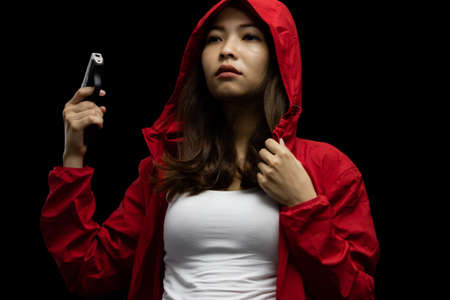 Portrait asian woman wearing a red coat one hand holding a pistol gun on black backgroundの写真素材
