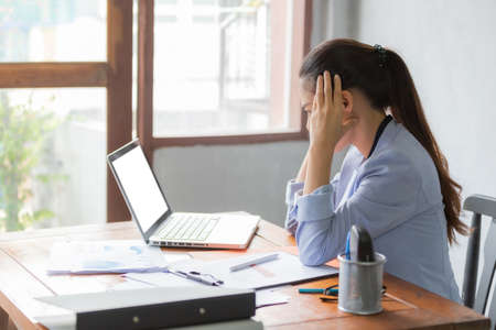 Asia business women feeling headache and stress. She is working at the office desk in front of laptop. Business and finance concept.の写真素材