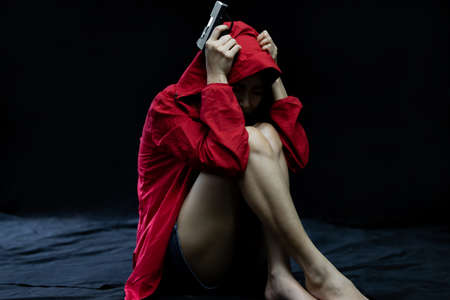 Hopeless Woman in violence with gun in hand sitting in dark room. The concept of stressed womanの写真素材