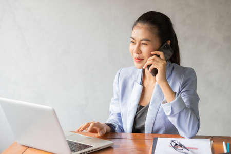 Business asian woman working on laptop at office while talking on phone and see information from laptop.の写真素材
