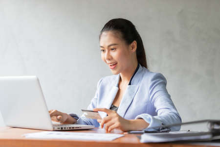 Young asian woman using credit card and laptop for online shopping at home office, smile and happy feeling businesswoman lifestyle conceptの写真素材