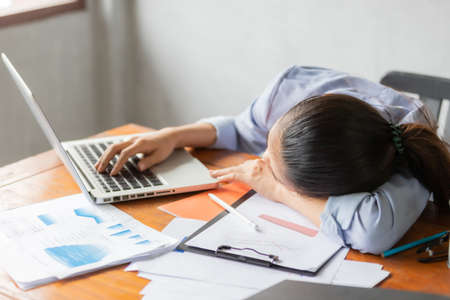 Asia business women feeling sleepy after long time working at the office desk in front of laptop. Business and finance concept.の写真素材