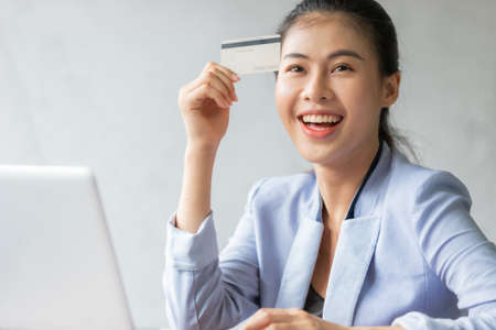 Young asian woman using credit card and laptop for online shopping at home office, smile and happy feeling businesswoman lifestyle conceptの写真素材