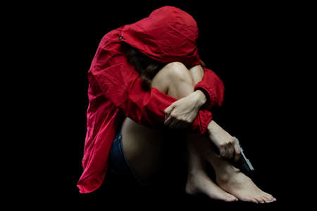 Hopeless Woman in violence with gun in hand sitting in dark room. The concept of stressed womanの写真素材
