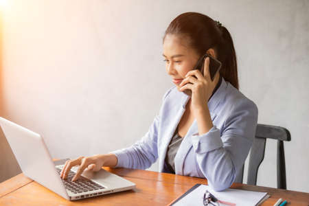 Business asian woman working on laptop at office while talking on phone and see information from laptop.の写真素材