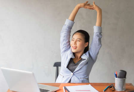 Business women or working lady are stretch oneself or lazily for relaxation on her desk while doing her work in the office.の写真素材
