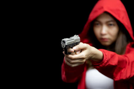 Portrait asian woman wearing a red coat one hand aiming a pistol gun on black backgroundの写真素材