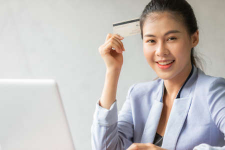 Young asian woman using credit card and laptop for online shopping at home office, smile and happy feeling businesswoman lifestyle conceptの写真素材